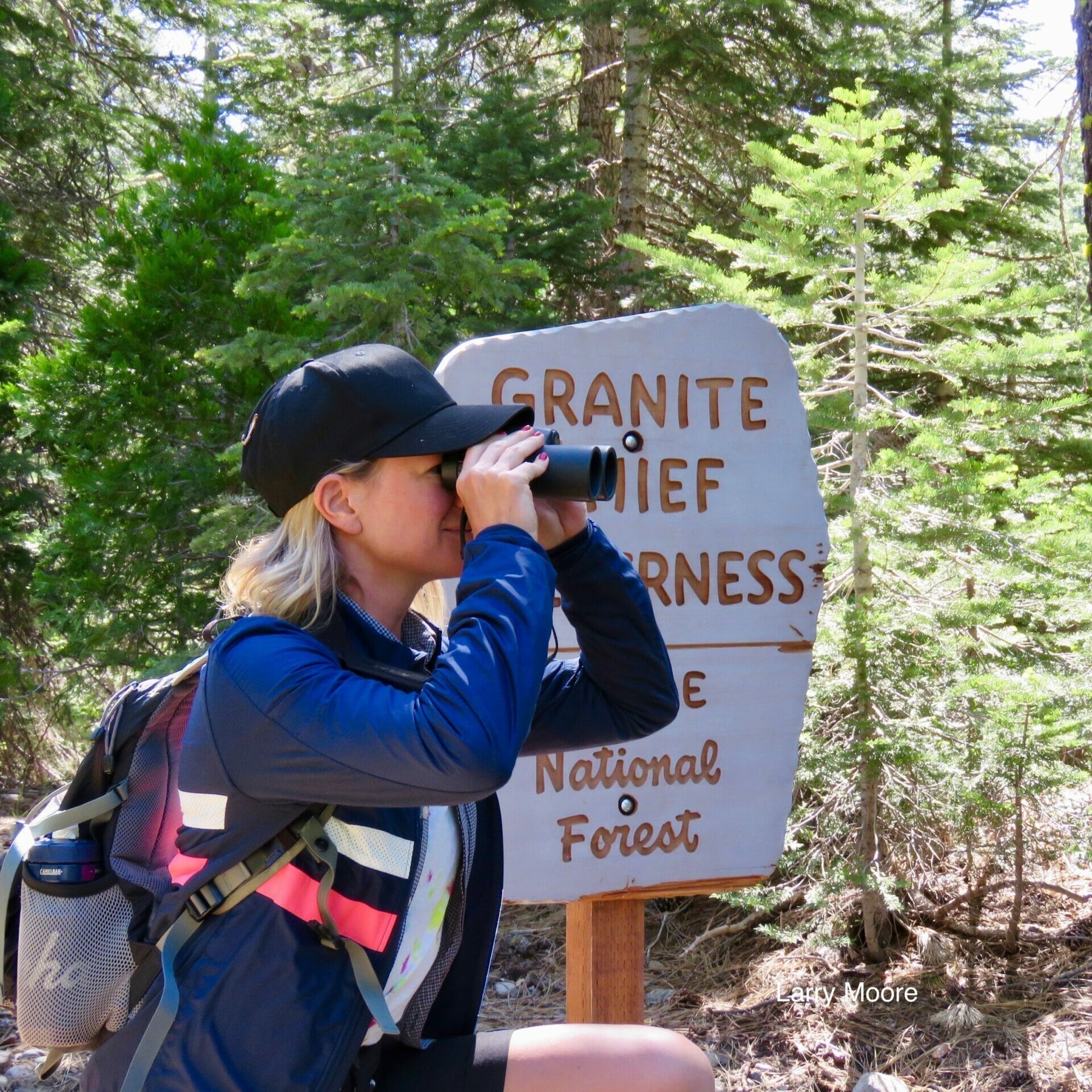 A hiker at the Granite Chief Wilderness sign, scanning the canyon with binoculars.